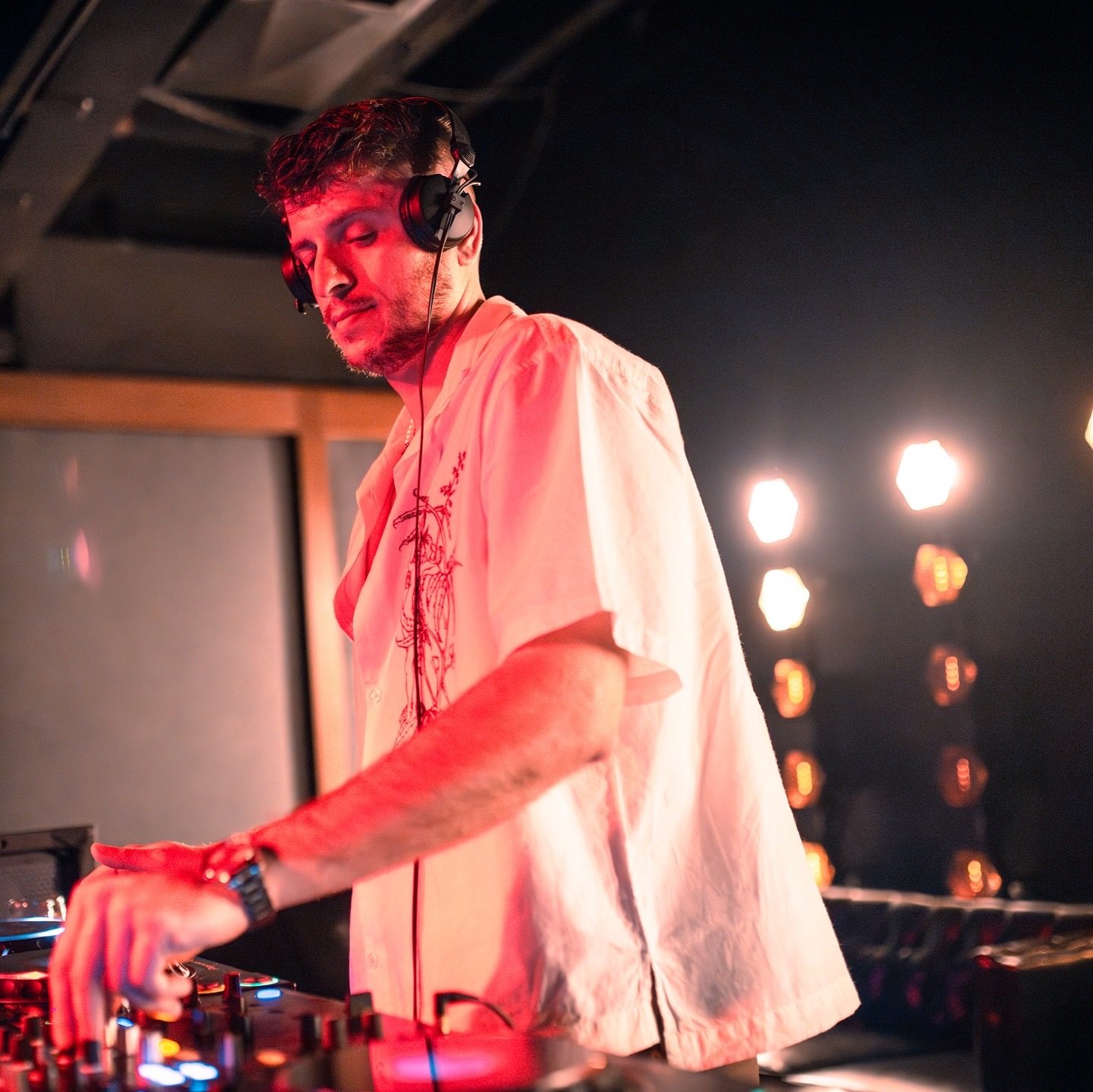 Adrian G working the decks, headphones on, red-lit