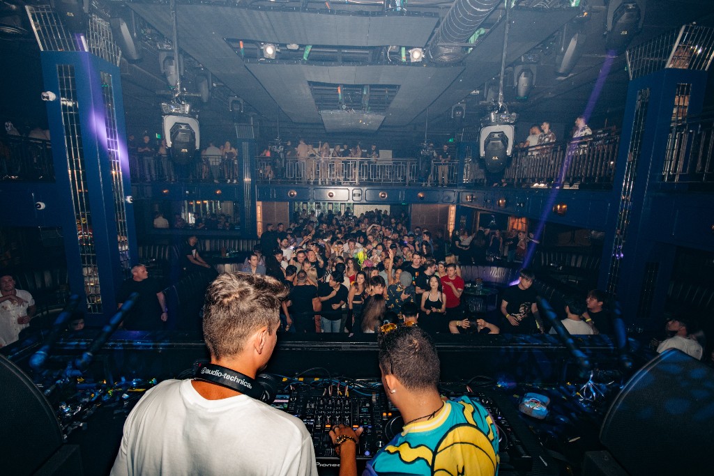 View from behind the DJs toward a packed club crowd